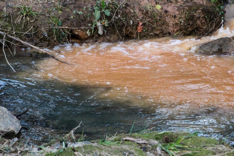 Darker water from Richland Creek meets water filled with red clay from Arcadia Drive runoff after a storm in Greenville, S.C.