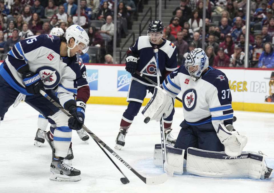 Winnipeg Jets defenseman Brenden Dillon, front left, blocks Colorado Avalanche right wing Mikko Rantanen, back left, as his shot on the net is stopped by Jets goaltender Connor Hellebuyck during the third period of an NHL hockey game Thursday, Dec. 7, 2023, in Denver. (AP Photo/David Zalubowski)