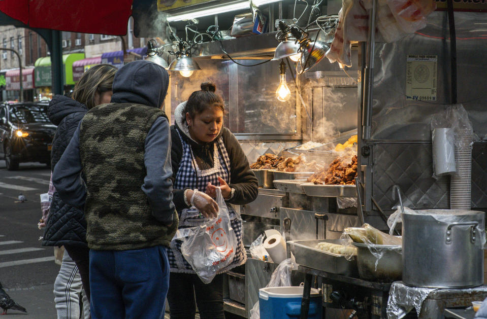 People buy food from a street cart attended by an Ecuadorian vendor, Monday, Feb. 27, 2023, in the Queens borough of New York. Ecuador — long known for remarkably low rates of crime, despite sitting in South America's cocaine heartland — has been struggling economically, fighting higher violence and losing its people in record numbers. Many are headed to the U.S. (AP Photo/Eduardo Munoz Alvarez)