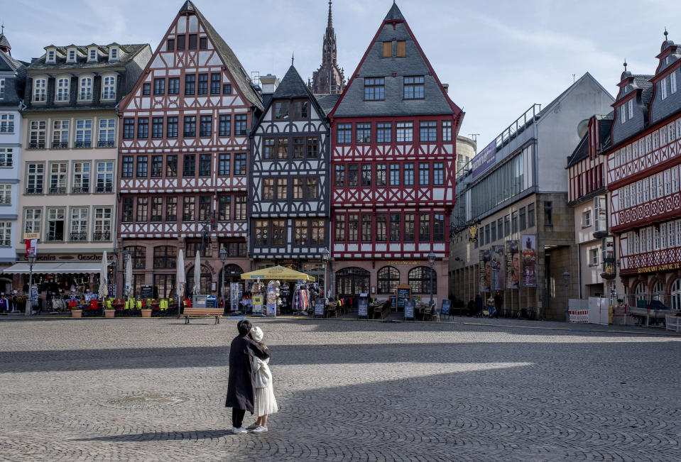 FILE - In this March 15, 2020 file photo, an Asian couple looks at timberframe houses at the almost empty Roemerberg square, the main tourist spot in Frankfurt, Germany. More than 50,000 people have died after contracting COVID-19 in Germany, a number that has risen swiftly over recent weeks as the country has struggled to bring down infection figures. (AP Photo/Michael Probst, File)