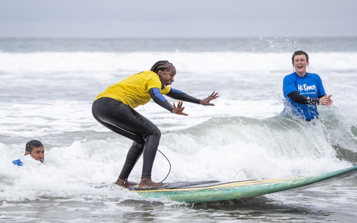A woman flings out her hands as she gets her balance on a surfboard