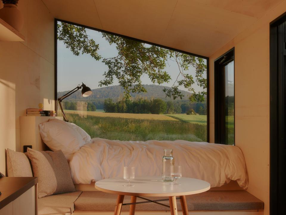 A bed and dining table next to a large window showing the view of nature