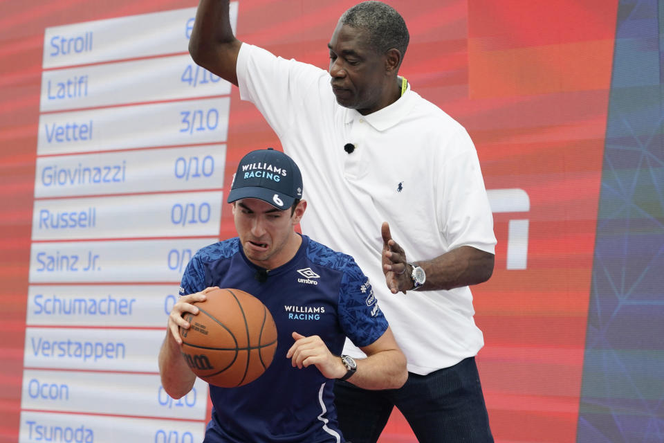 Williams driver Nicholas Latifi, of Canada, left, tries to drive around former NBA player Dikembe Mutombo at the Formula One U.S. Grand Prix auto race at the Circuit of the Americas, Thursday, Oct. 21, 2021, in Austin, Texas. F1 Teams took part in a free throw challenge as to help the NBA celebrate their 75th Anniversary. (AP Photo/Eric Gay)