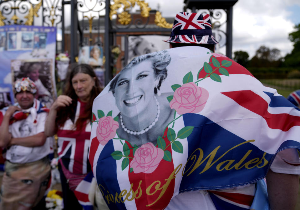 People wave a flag as they stand in front of messages of remembrance for Princess Diana outside the gates of Kensington Palace, in London, Wednesday, Aug. 31, 2022. Wednesday marks the 25th anniversary of Princess Diana's death in a Paris car crash. (AP Photo/Alastair Grant)