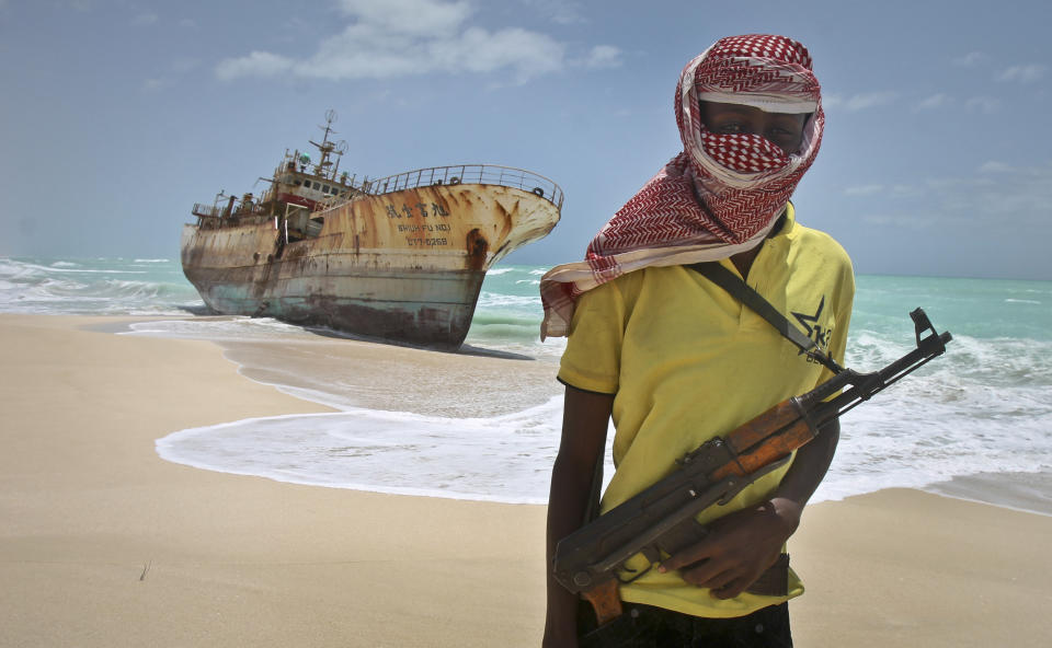 FILE - In this Sunday, Sept. 23, 2012 file photo, masked Somali pirate Hassan stands near a Taiwanese fishing vessel that washed up on shore after the pirates were paid a ransom and released the crew, in the once-bustling pirate den of Hobyo, Somalia. World sea piracy fell for a third straight year in 2013, as Somali pirates were curbed by international naval patrols and improved ship vigilance, an international maritime watchdog said Wednesday, Jan. 15, 2014. (AP Photo/Farah Abdi Warsameh, File)