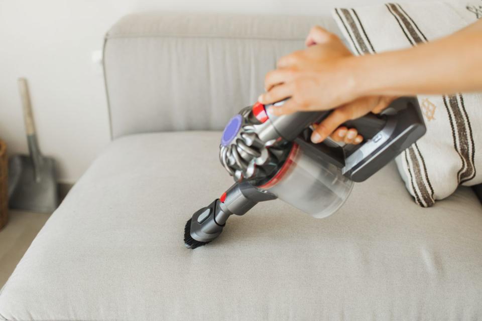 small portable vacuum cleaner in woman hands vacuuming dust on sofa