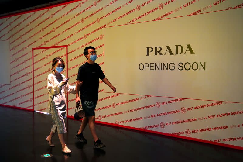 People wearing face masks following the COVID-19 outbreak walk past a store of Italian luxury brand Prada to open soon inside a shopping mall in Beijing