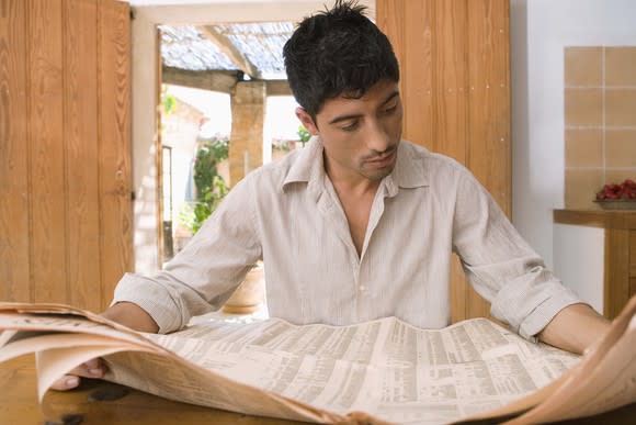 A middle-aged man reading the financial section of the newspaper at a table.