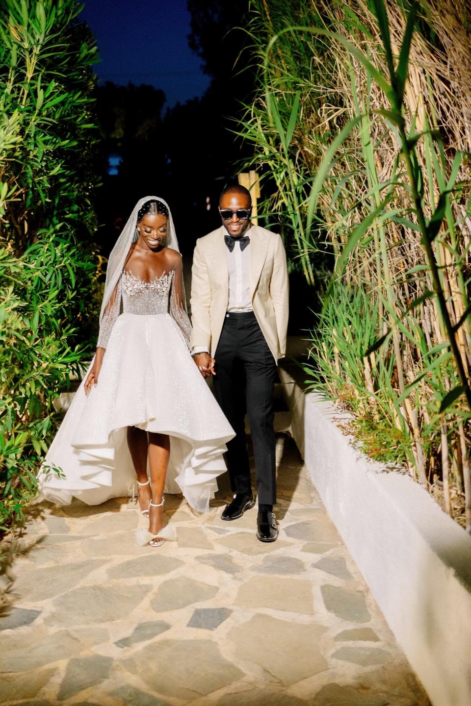 A bride and groom hold hands and laugh as they walk down a cobblestone path at night.