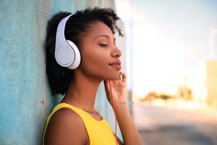 A woman leaning against a wall wearing a large pair of headphones.