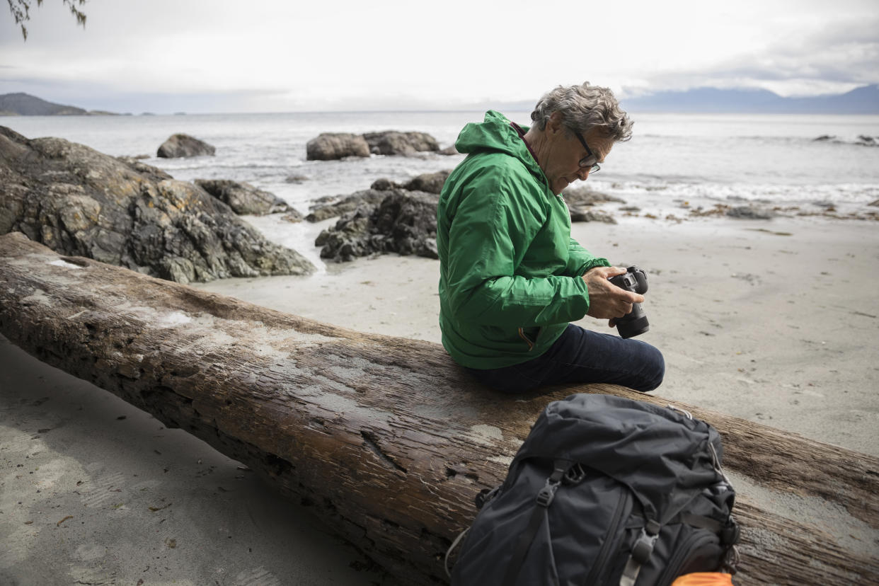 Active senior male backpacker using camera on rugged beach