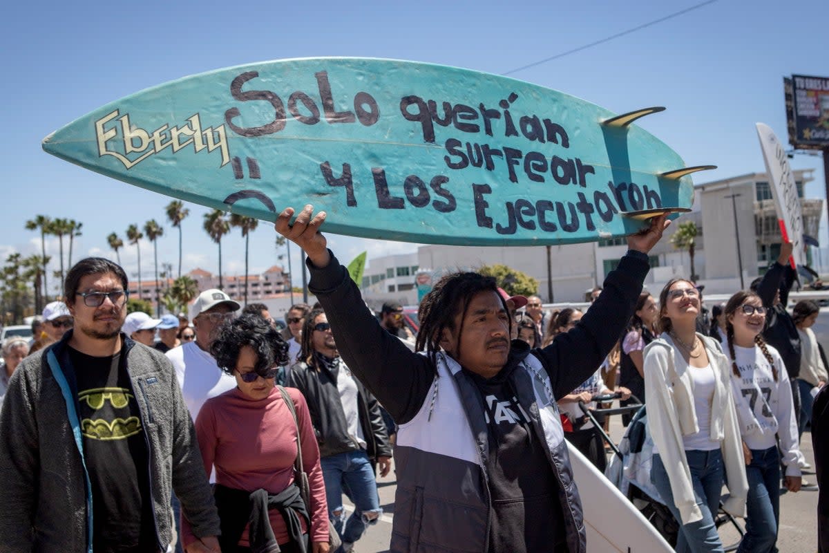 A demonstrator holding a bodyboard written in Spanish ‘They just wanted to surf and they were executed’ (AP)