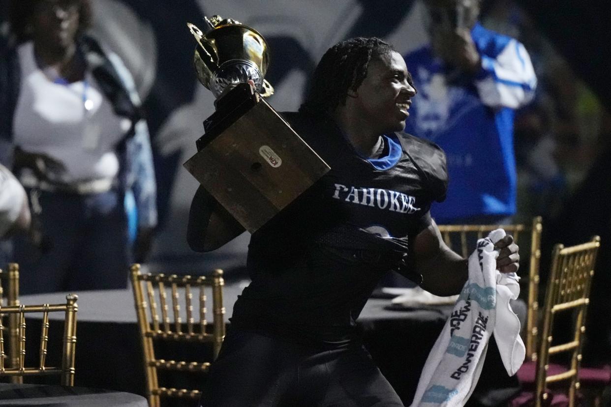 Jenorris Wilcher Jr. grabs the Muck Bowl trophy following the high school football game against Glades Central at Pahokee High School in Pahokee, Florida, Nov. 3, 2023.