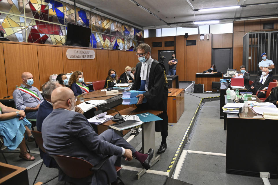 Roberto Capra, center, lawyer of Finnegan Lee Elder, hands over the files containing the psychiatric evaluation papers to psychiatric experts Vittorio Fineschi and Stefano Ferracuti, back to camera, during trial for the killing of Italian Carabinieri police officer Mario Cerciello Rega, in Rome, Wednesday, July 22, 2020. Court-appointed psychiatrists testified on Wednesday that a young Californian man, accused of murdering an Italian police office, suffers from anxiety, depression and “a sense of chronic anger” but is competent to stand trial. A psychiatric evaluation was requested by defense lawyers for Finnegan Lee Elder, 20, on trial in Rome since February for the slaying of a plainclothes Carabinieri police officer. (Andreas Solaro/Pool via AP)
