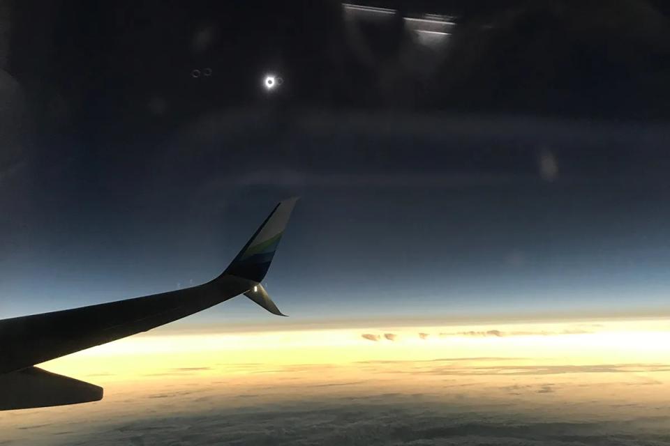 a view of a distant solar eclipse over clouds and an airplane wing