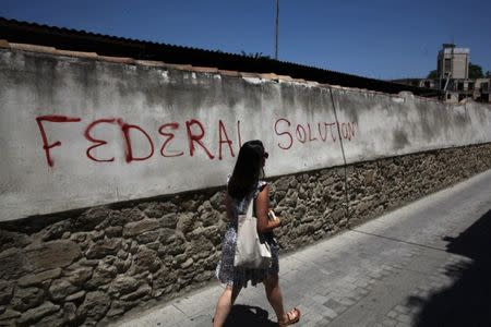 A woman walks past graffiti near the United Nations Buffer Zone in Nicosia, Cyprus June 28, 2017. REUTERS/Yiannis Kourtoglou