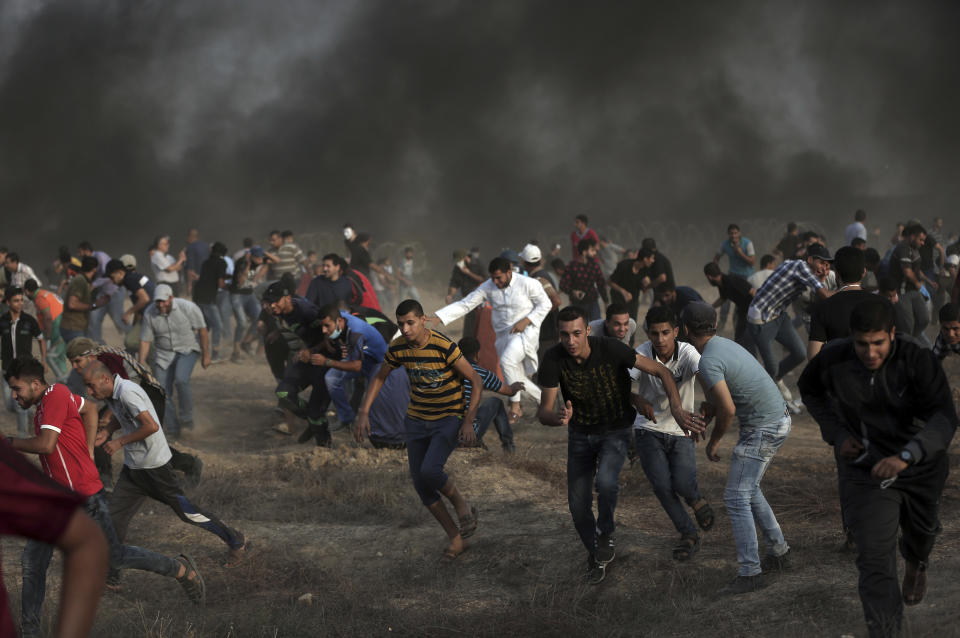 Palestinian protesters run for cover from teargas fired by Israeli troops during a protest at the Gaza Strip's border with Israel, Friday, Oct. 19, 2018. (AP Photo/Khalil Hamra)