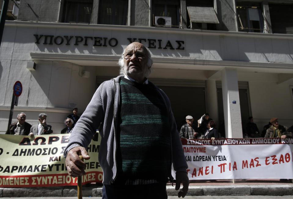 A pensioner stands outside the Health Ministry as the banners read ''Free Health Care'' during a rally in Athens, on Thursday, March 20, 2014. Hundreds of elderly Greeks who have faced successive pension cuts since Greece began relying on international rescue loans in 2010, and have also been hard hit by health care cuts, took part in the rally. Greek civil servants, including hospital and teaching staff, have started a two-day strike on Wednesday against austerity measures imposed under the debt-mired country's international bailout commitments. (AP Photo/Thanassis Stavrakis)