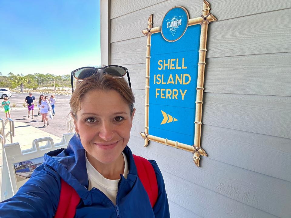Selfie of the writer wearing a blue jacket in front of a blue sign that reads "Shell Island Ferry" in yellow letters