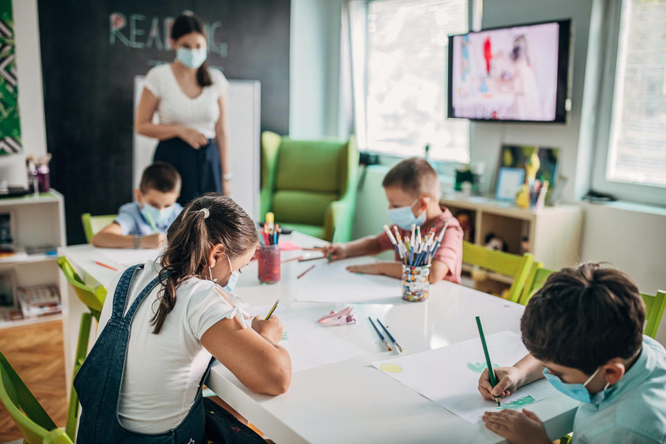 A teacher standing next to a table of children drawing