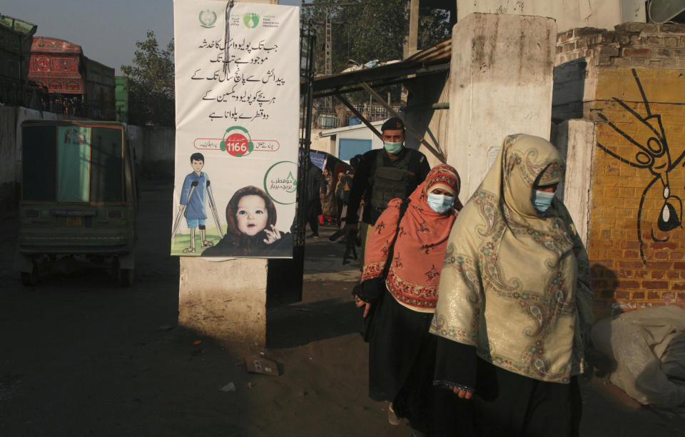 A police officer escorts health workers arriving to administrate polio vaccine in a slum area of Peshawar, Pakistan, Monday, Jan. 24, 2022. Pakistani authorities launched the year's first anti-polio campaign even as coronavirus cases suddenly rise in an effort to eradicate the crippling children's disease. (AP Photo/Muhammad Sajjad)
