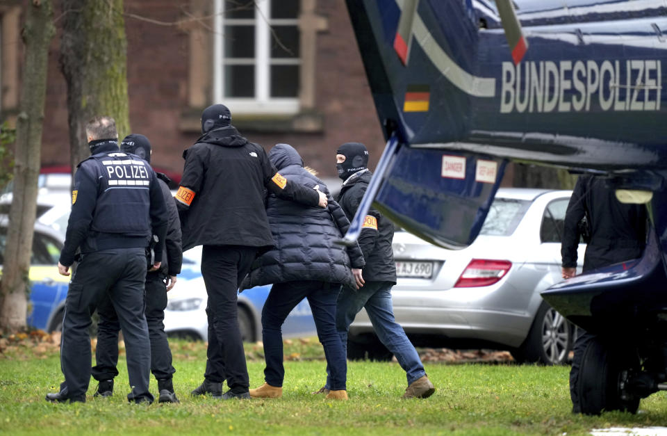 An suspect, second right, is escorted from a police helicopter by police officers after the arrival in Karlsruhe, Germany, Wednesday, Dec. 7, 2022. Thousands of police officers carried out raids across much of Germany on Wednesday against suspected far-right extremists who allegedly sought to overthrow the government in an armed coup. Officials said 25 people were detained. (AP Photo/Michael Probst)