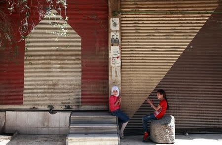 Syrian girls sit in front of shops in the rebel held besieged Douma neighbourhood of Damascus, Syria July 23, 2017. REUTERS/Bassam Khabieh