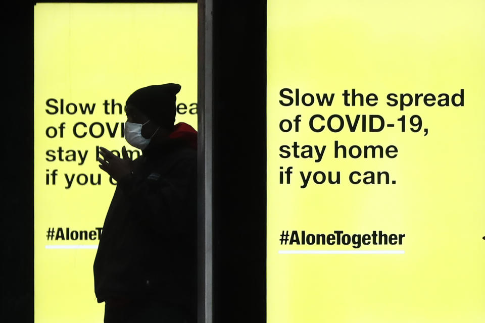 A pedestrian waits in silhouette for a Chicago Transit Authority bus as several COVID-19 public service messages are projected on screens at the bus stop Thursday, April 30, 2020, in Chicago.  (AP Photo/Charles Rex Arbogast)