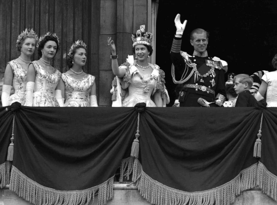 Britain's Queen Elizabeth II and Prince Philip wave from a balcony while three women watch nearby.