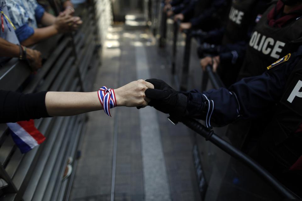 An anti-government protester holds hands with an anti-riot policemen across the closed gates outside the headquarters of the ruling Puea Thai Party of Prime Minister Yingluck Shinawatra in Bangkok