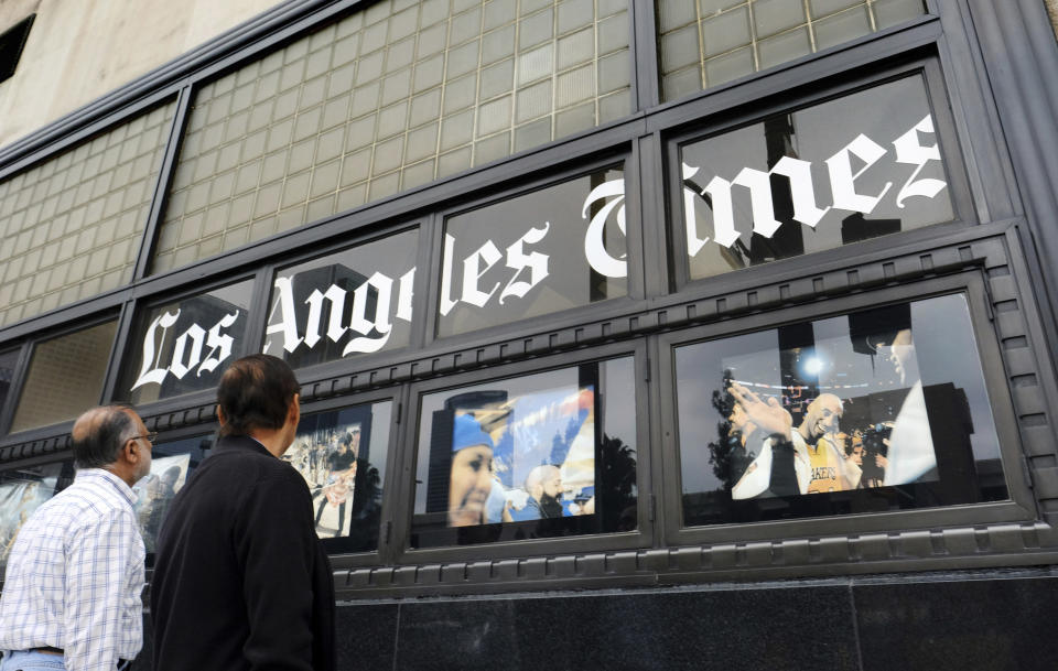 FILE - In this May 16, 2016, file photo, pedestrians look at news photos posted outside the Los Angeles Times building in downtown Los Angeles. A computer virus hit newspaper printing plants in Los Angeles and at Tribune Publishing newspapers across the country. The virus that hit Los Angeles prevented it from printing and delivering Saturday editions of the Los Angeles Times, the San Diego Union-Tribune and other papers to some subscribers. (AP Photo/Richard Vogel, File)