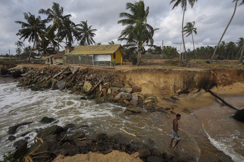 Nuwan Fernando stands between a washed out stretch of land in his backyard on an eroding coast in Iranawila, Sri Lanka, Thursday, June 15, 2023. "I don't know what will happen in the future but I still keep my faith," Fernando said, one of a few in Iranawila whose house remains intact. (AP Photo/Eranga Jayawardena)