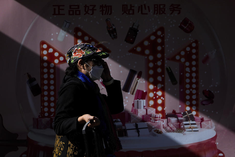 A woman wearing a face mask talks on her phone as she walks by an online shopping day, known as "Singles' Day" advertisement on display at a bus stand in Beijing, Wednesday, Nov. 10, 2021. China's biggest online shopping day, known as "Singles' Day" on Nov. 11, is taking on a muted tone this year amid a regulatory crackdown on the technology industry and President Xi Jinping's push for "common prosperity." (AP Photo/Andy Wong)