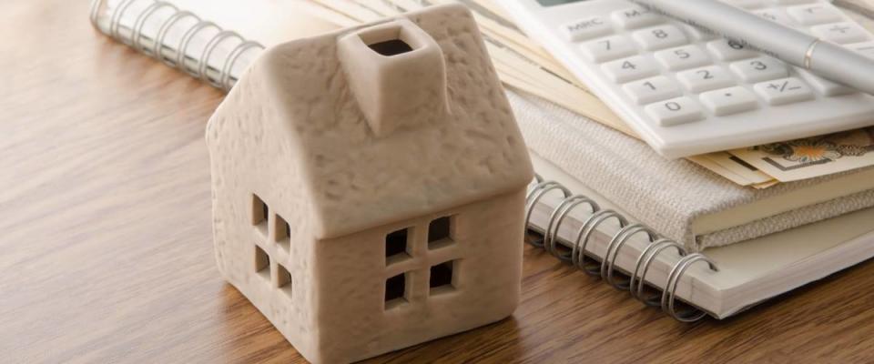 Mold of a house on desk, with refinancing plans and calculator on the side