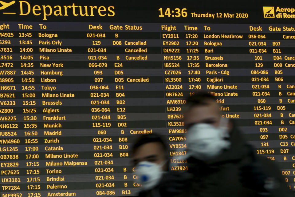 People walk by a departures monitor at the Rome Leonardo da Vinci International Airport, Thursday, March 12, 2020. Airlines and travelers are still sorting out the new travel ban that President Donald Trump announced late Wednesday, barring most foreign visitors from continental Europe for 30 days. (AP Photo/Andrew Medichini, File)