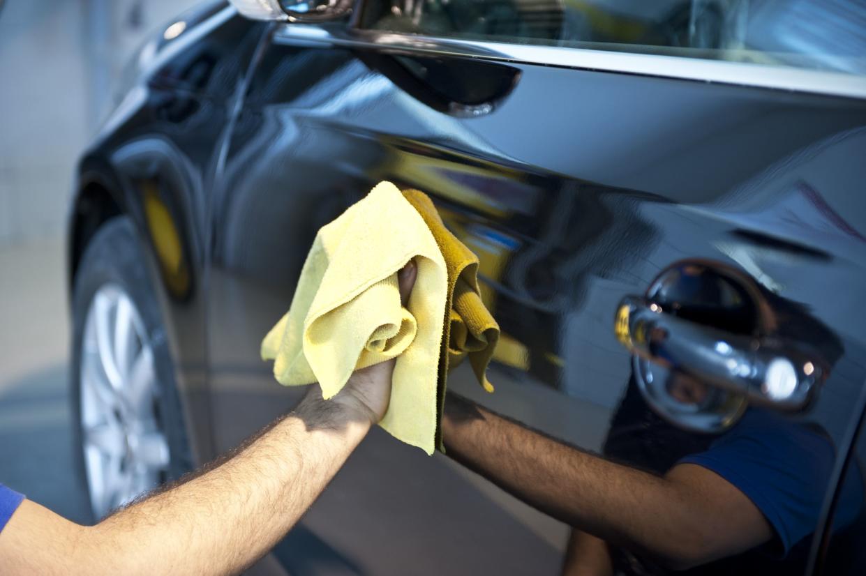 Close up of a man wiping a black car with a yellow microfiber cloth