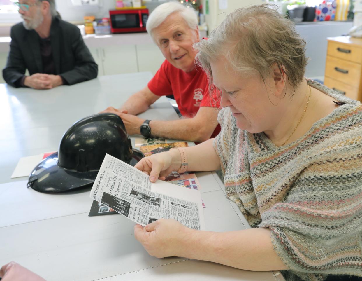 Christina Surgeon reads a newspaper article from 1972, when she survived a fire fought by Akron firefighters David Sullivan, left, and Larry Steele. Surgeon was 1 when the fire broke out, killing her mother.