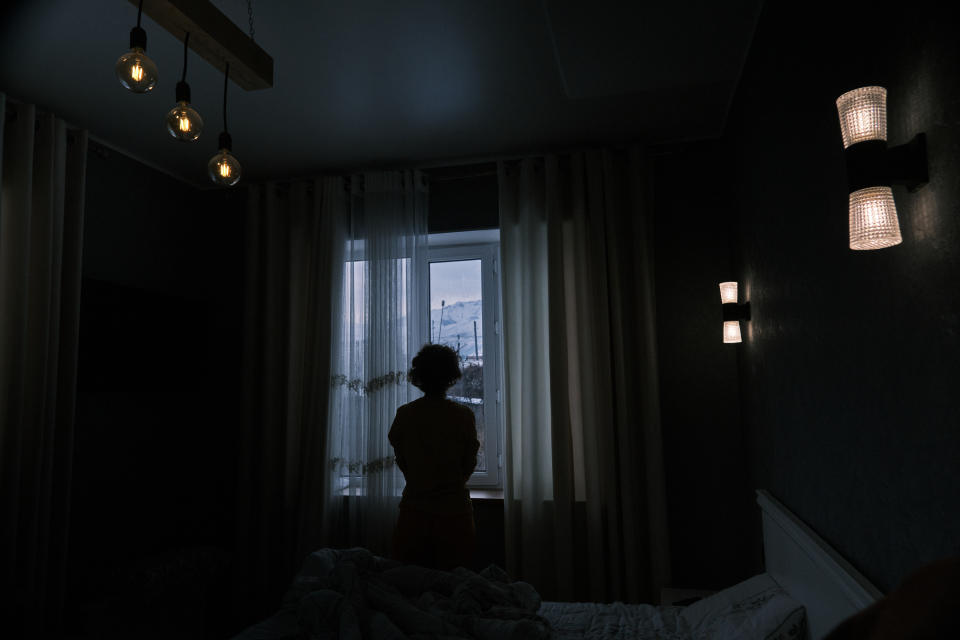 Mature woman is exercising next to the window in the dark bedroom