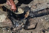 A man uses an old fan as a grill to prepare food for his family at Bahia de los Ninos beach in La Guaira