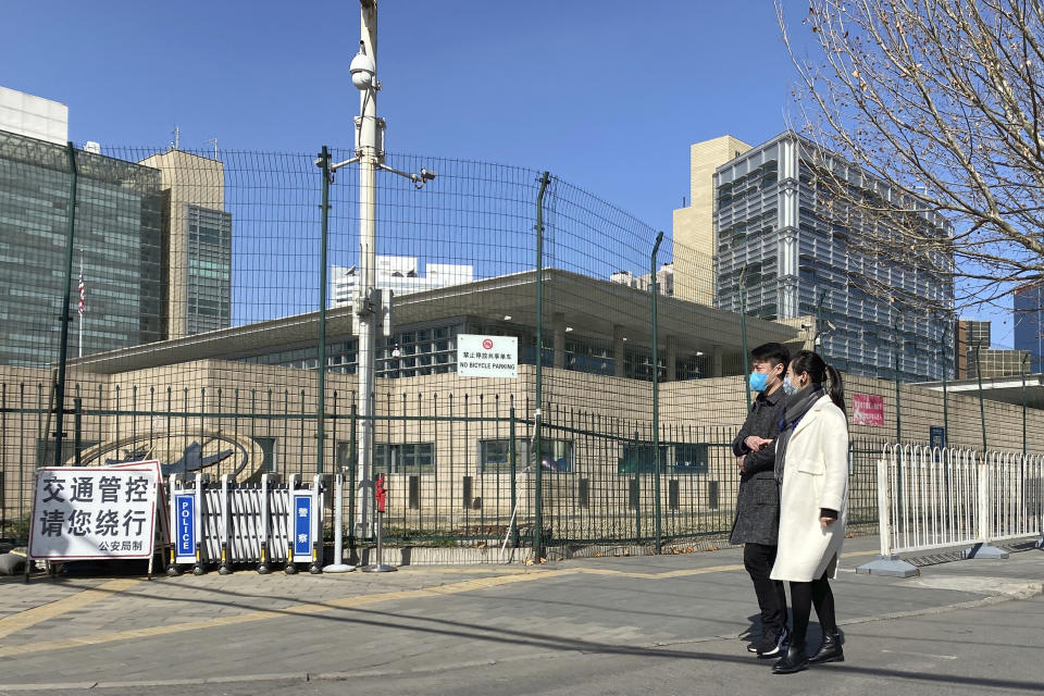 In this Thursday, March 12, 2020, photo, a man and a woman wearing masks walk past the U.S. embassy in Beijing. After American consulates in China suspended visa processing amid the coronavirus outbreak, hundreds of Chinese citizens applying for U.S. work visas have been stuck in limbo, fretting as crucial deadlines loom and their jobs in America look increasingly at risk. (AP Photo/Ng Han Guan)