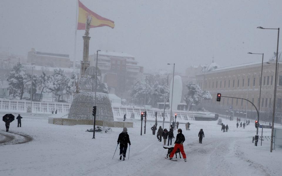 A man skis in Colon square in front of the statue of Christopher Columbus and a large Spanish flag during a heavy snowfall in central Madrid - AP