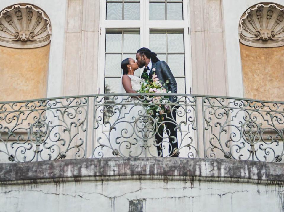 A bride and groom kiss in front of a mansion.