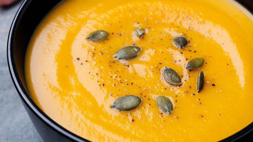 pumpkin cream soup with pumpkin seeds in a black bowl