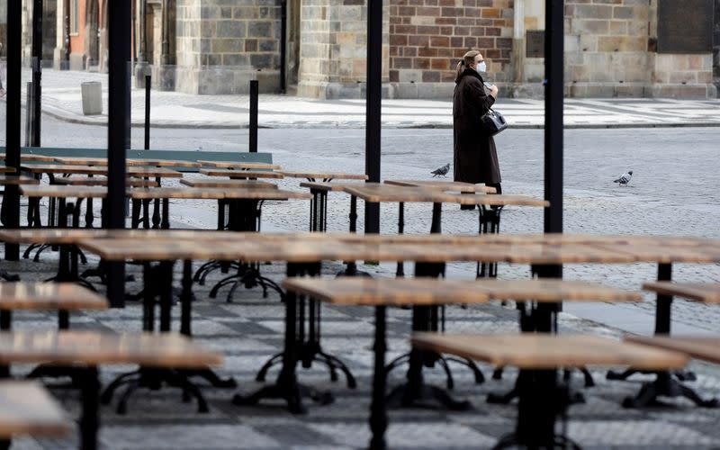 IMAGEN DE ARCHIVO. Una mujer utilizando una mascarilla camina cerca de mesas vacías de un restaurante en Praga, República Checa