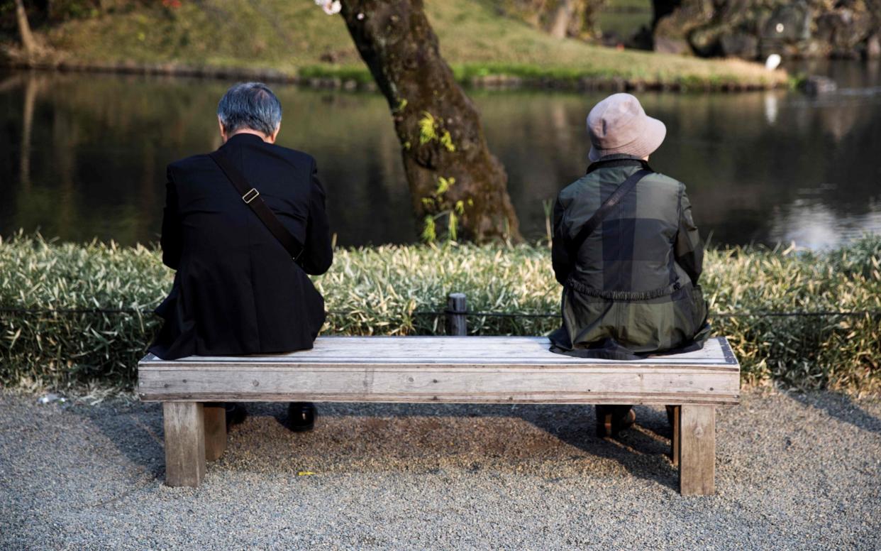 An elderly man and woman sit on a bench in a park in Tokyo (file photo) - AFP