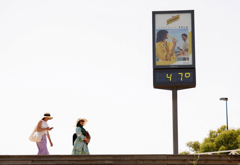 FOTO DE ARCHIVO: Mujeres caminan junto a un termómetro que muestra 47 grados Celsius durante la primera ola de calor del año en Sevilla