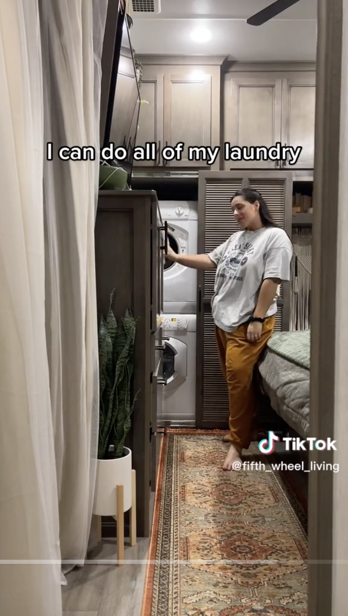 Kirs standing next to the stacked washer and dryer. The floor has a patterned area rug and there's a potted plant