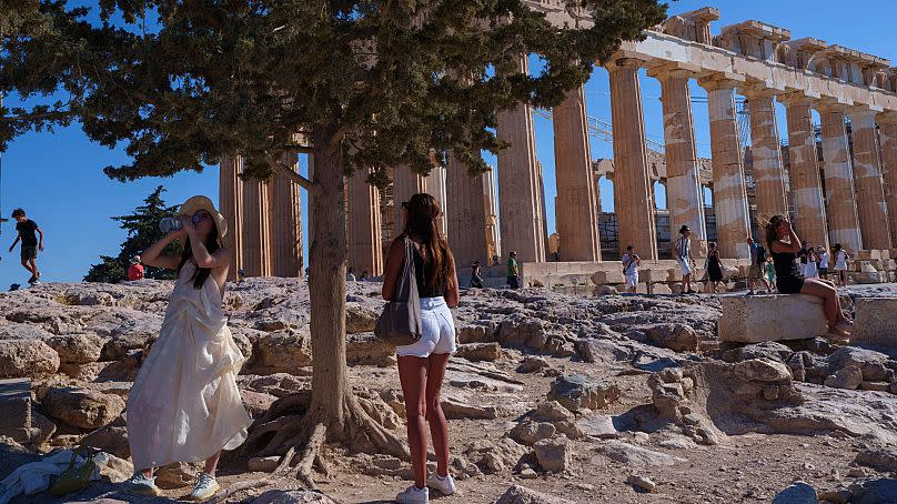 Una mujer bebe agua frente al antiguo templo del Partenón durante un día caluroso y ventoso en la colina de la Acrópolis, en Atenas, el martes 16 de julio de 2024.