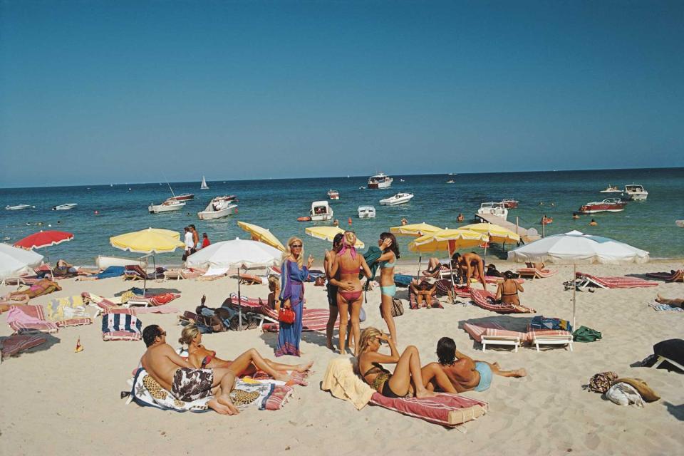 A crowd of chic beachgoers on a beach in St Tropez, photographed by Slim Aarons circa 1971