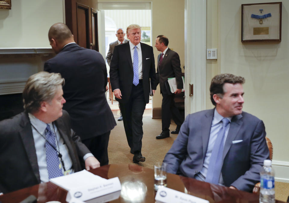 President Donald Trump walks in from the Oval Office of the White House in Washington in Washington, Monday, Jan. 23, 2017, before hosting breakfast with business leaders in the Roosevelt Room. Sitting at the table is White House Senior Adviser Steve Bannon, left, and Kevin Plank, founder, CEO and Chairman of Under Armour. (AP Photo/Pablo Martinez Monsivais)